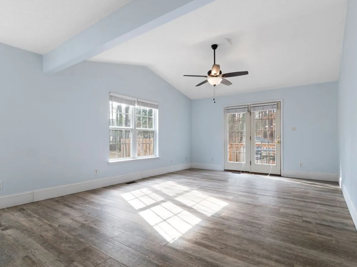 Empty sunlit room with a continuous wood-look floor and French doors