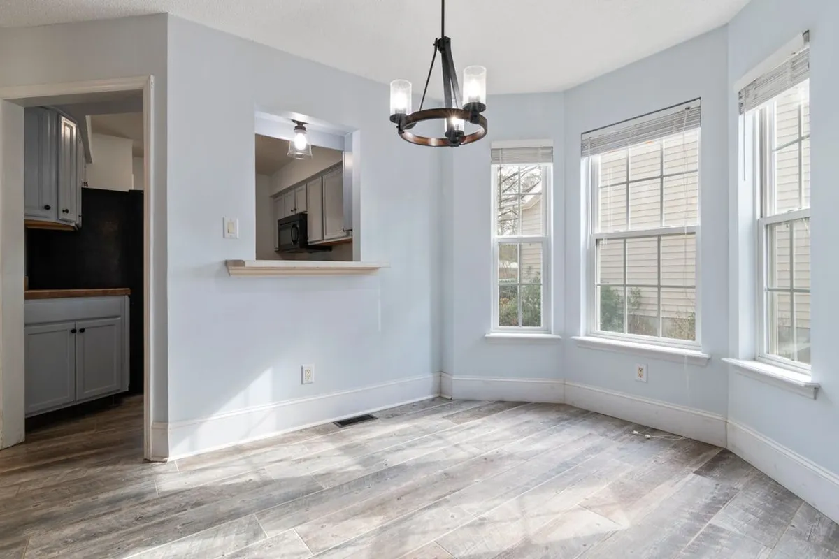 A sunny dining nook where the same wood-look floor runs unbroken from room to room — sheet vinyl is laid as one wide piece with few or no seams, which is why its labor is 35–50% of the budget while the sheet itself is 30–45%. Captions on this page describe the visible floors; the pictured floors are not certified as sheet vinyl.