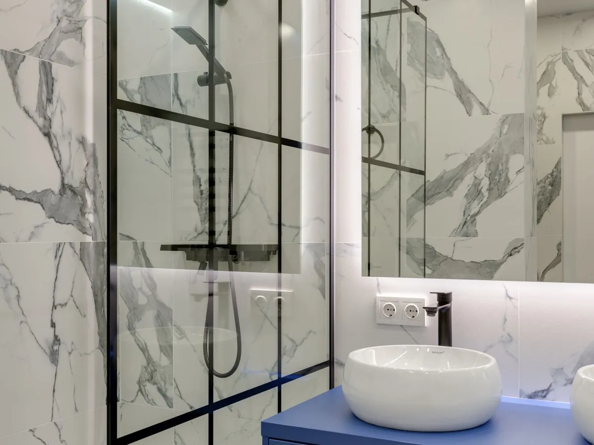 Black-framed glass shower enclosure with a rainfall shower over marble-look tile