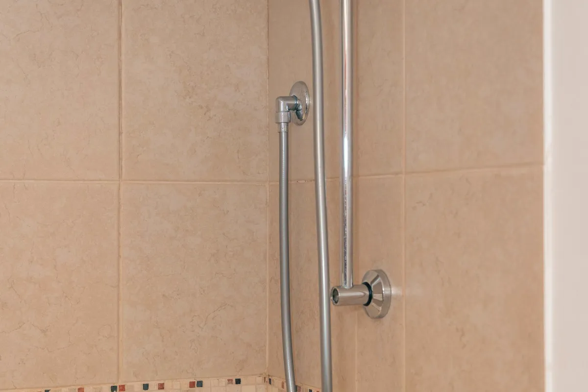 A chrome showerhead and fixture set on a tiled wall — the valve, head and trim are a modest share of a shower budget next to the tile, backer board and waterproofing labor behind them.