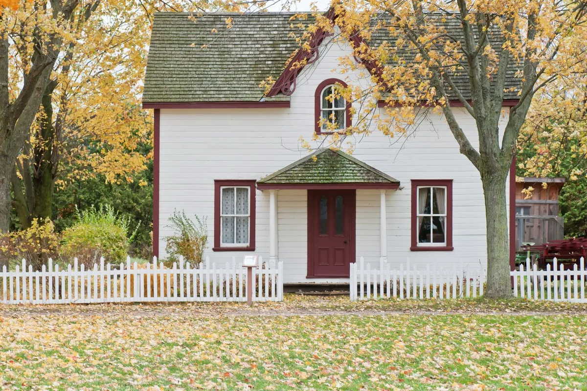 A white lap-sided house with contrasting trim and a picket fence — siding material and trim scope are the two lines that decide most of a replacement budget.