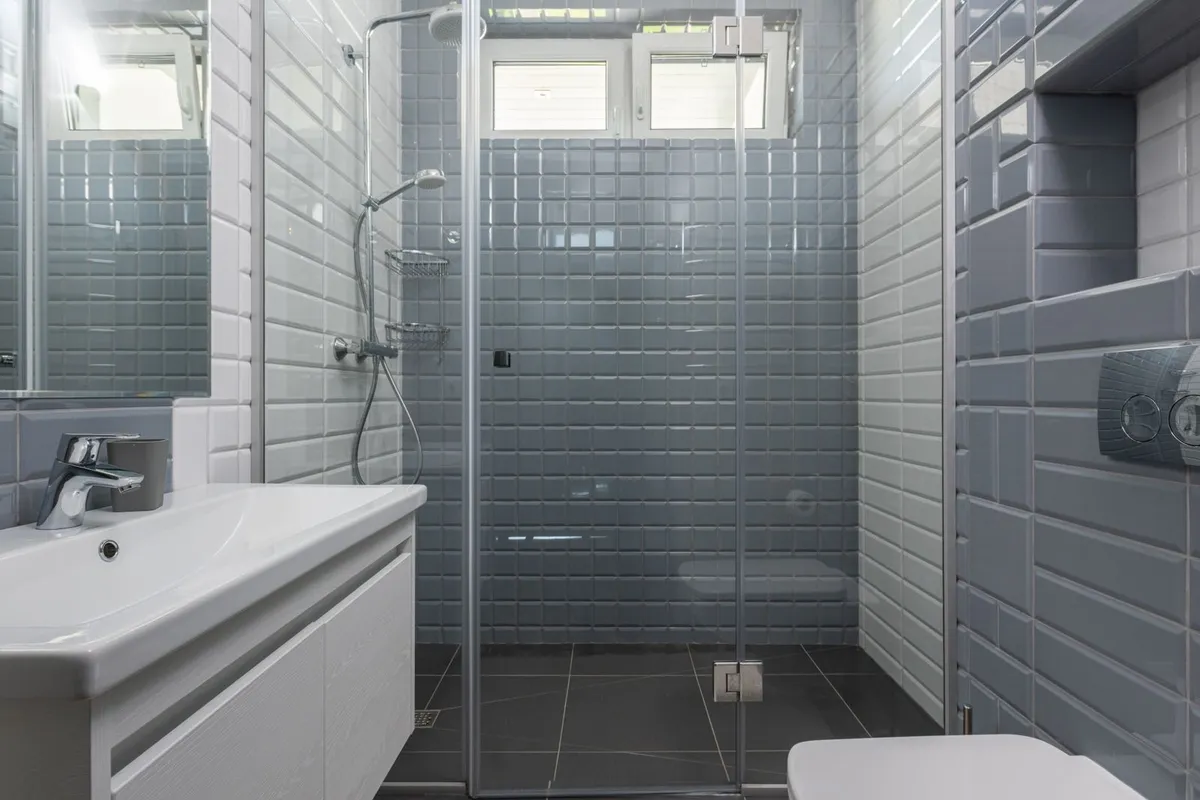 A glass shower standing on dark large-format stone-look floor tiles — wet-area stone tile is sealed before and after grouting, and that sealing sits in the breakdown above. Captions describe the visible tile only; the pictured floor is not certified as slate.