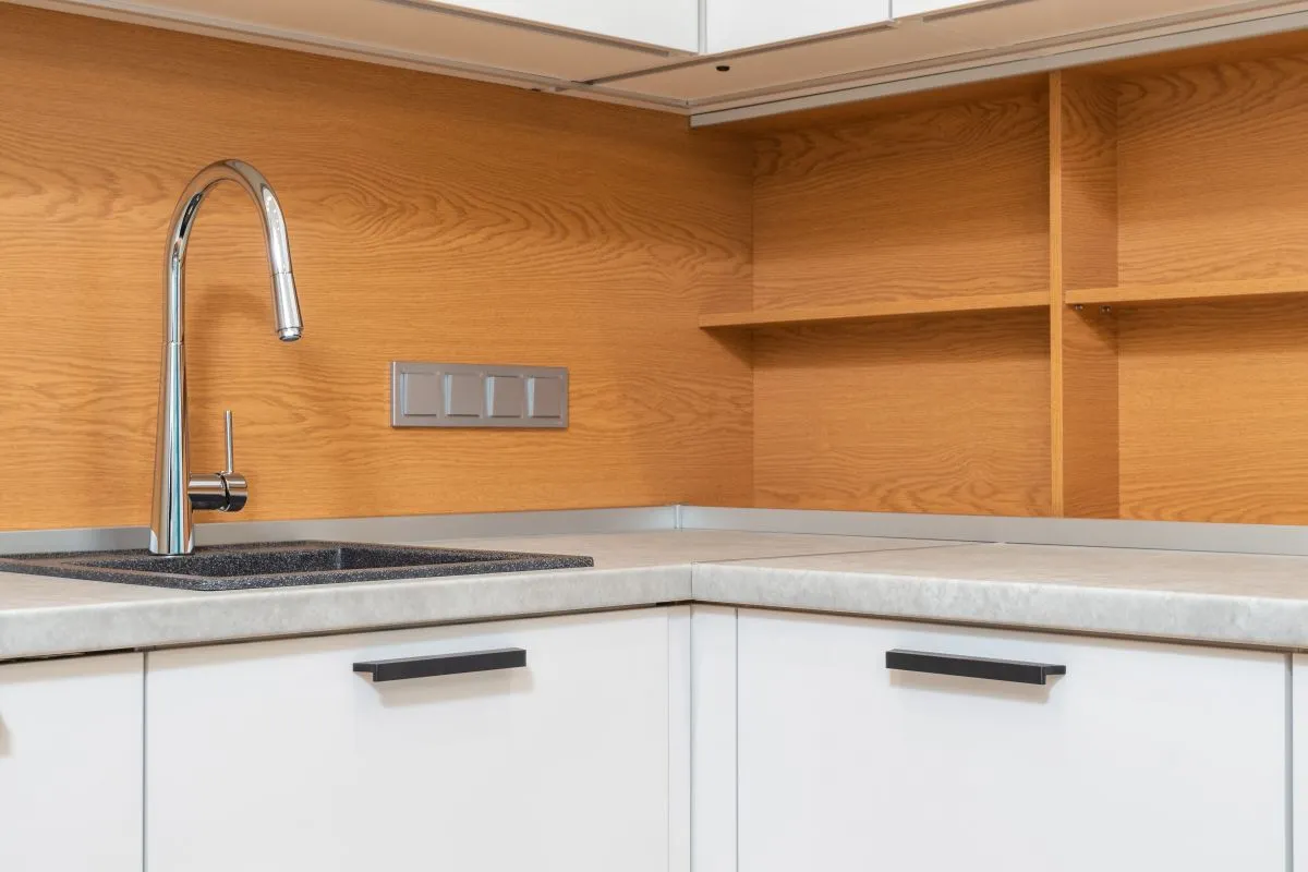 A sink set into a light counter in close view, with a tall faucet — solid surface can form its sink from the same sheet with no seam to clean, priced at $100–$300+ per integral sink in HomeGuide.