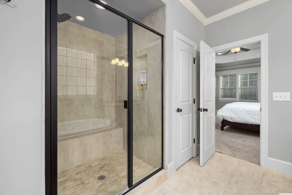 A glass-enclosed shower with stone tile — wet-area stone is sealed before and after installation, and that sealing is a recurring line: resealing runs $1–$3 per sq ft every one to three years in Angi's data.