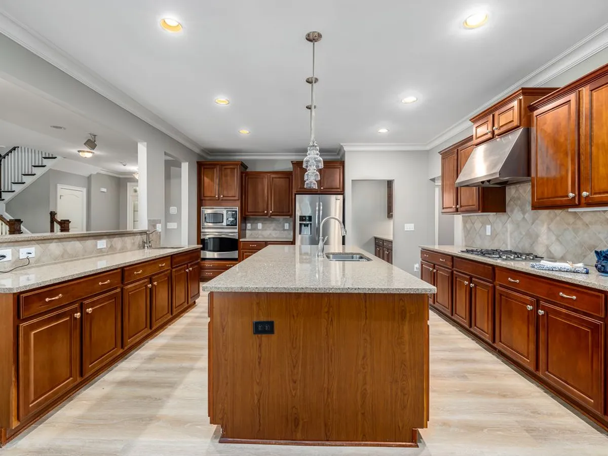 Long kitchen with wood cabinets, a central island and a light natural stone tile floor