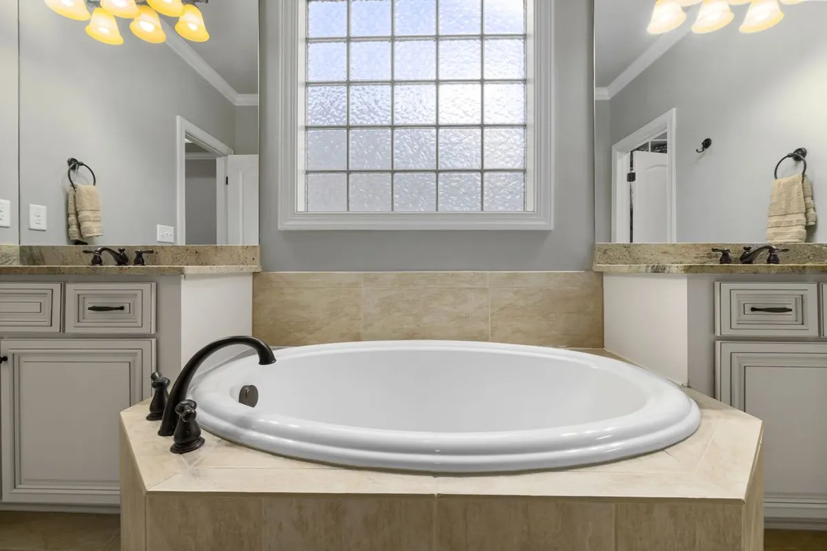 A bathroom with an oval tub set into a stone tile deck between two vanities — bathrooms and kitchens are where stone floors are most often installed, and stone tile material is 40–55% of a stone floor budget, so the stone chosen for a room like this sets most of the project total.