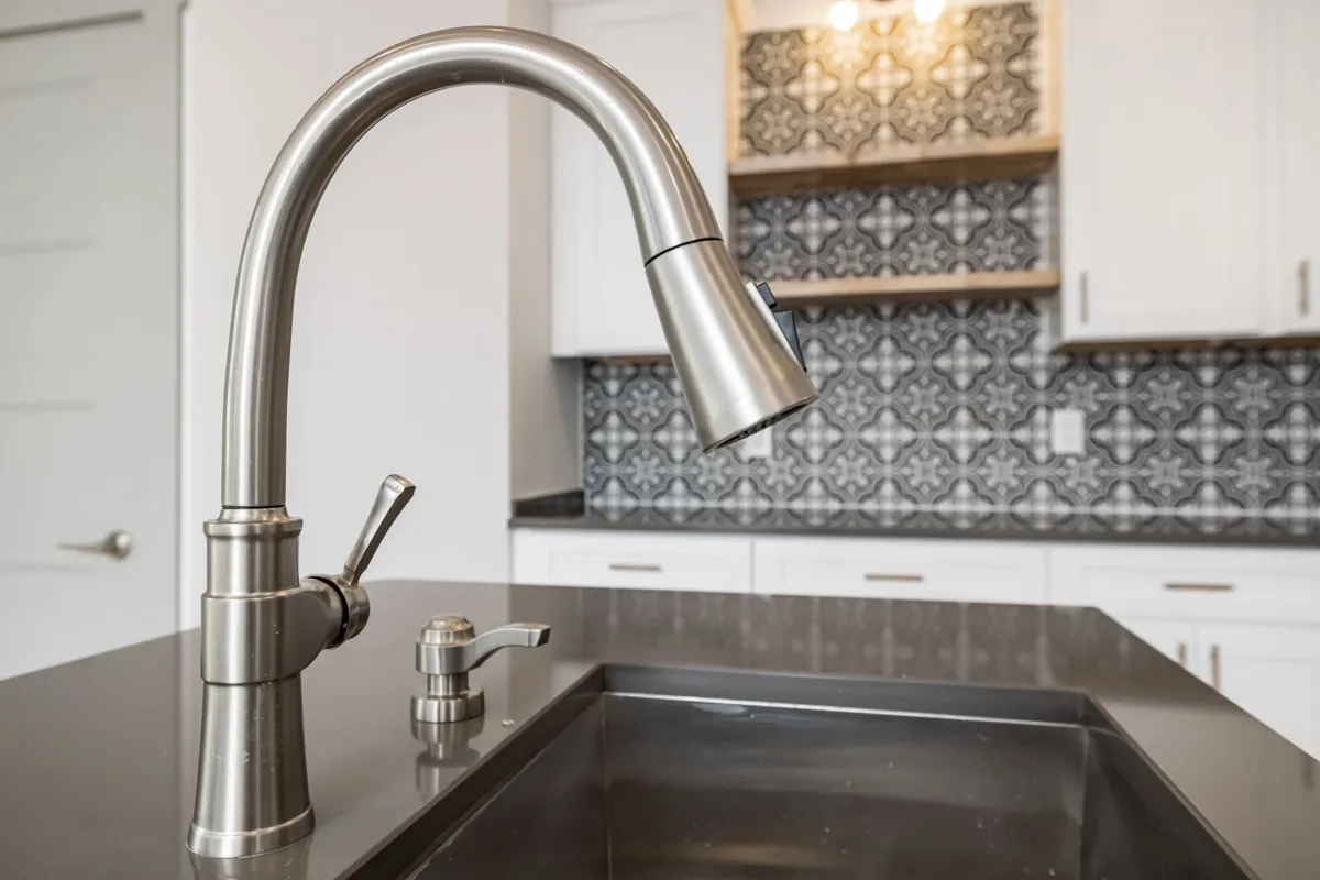 A sink set into a dark polished counter in close view — cutouts run $150 or more each beyond the standard sink and faucet in Angi, which is why the layout is fixed before the slab is cast.