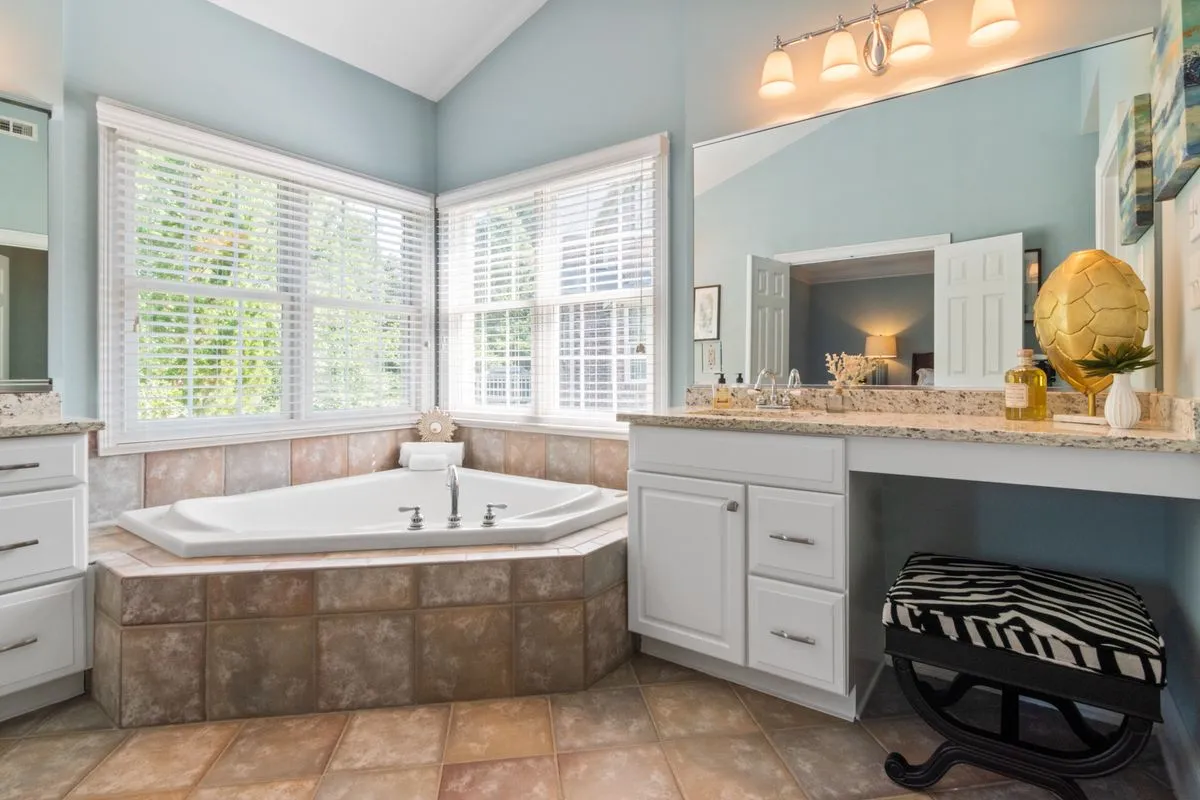A bathroom corner tub set into a large-format stone-look tile deck — tile counters are built the same way this deck is: piece by piece on a rigid backer base, with the grout joints sealed.