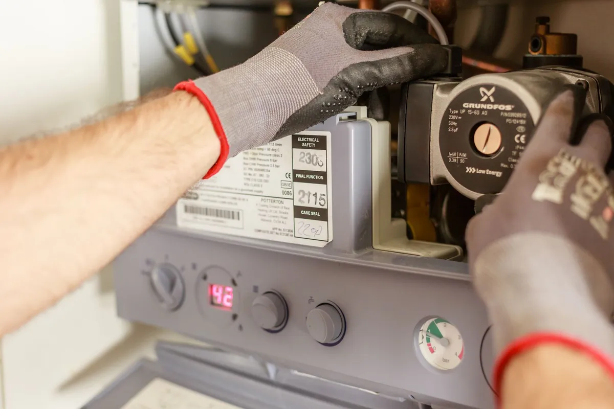 Gloved hands adjusting the controls and pump inside a water heater unit — the unit itself is 40–55% of a typical replacement budget, before labor and code-required parts.