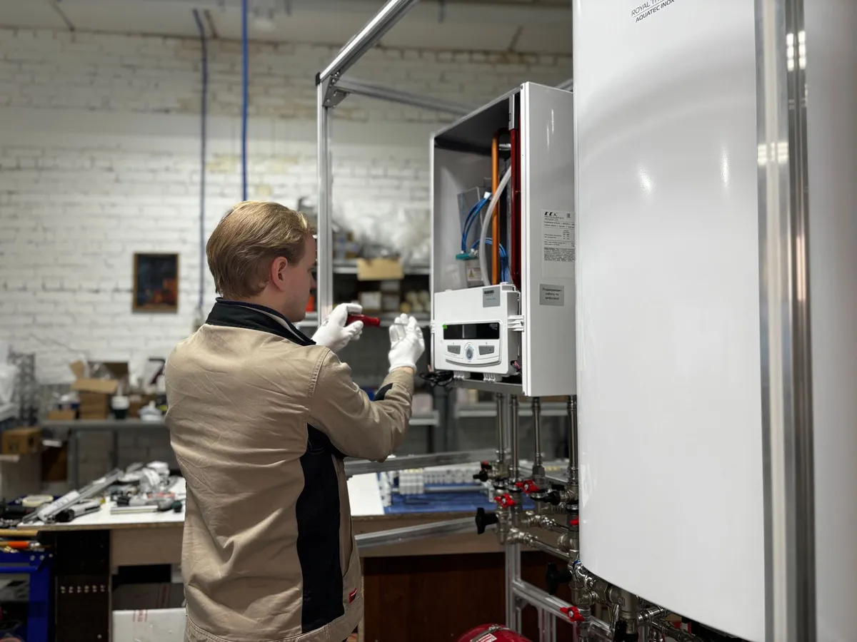 Technician servicing a wall-mounted tankless water heater with its cover open