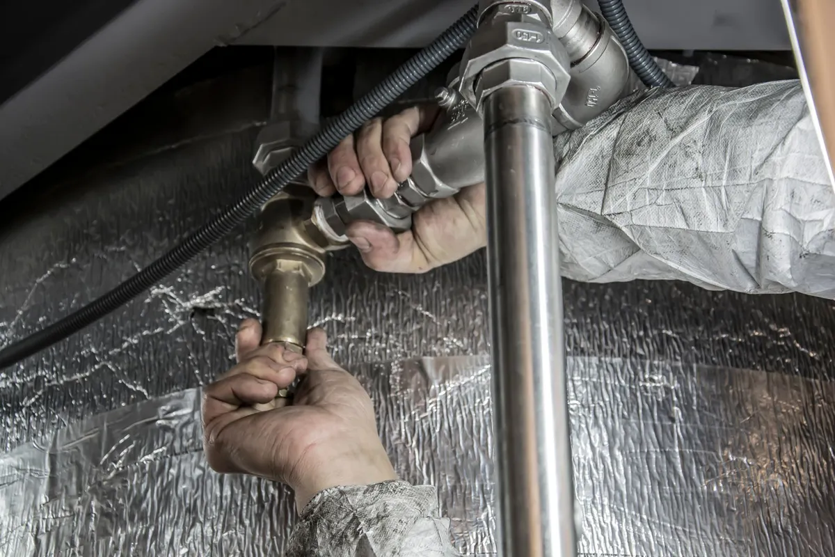Hands connecting pipework and valves during a water heater installation — installation labor is 30–45% of a replacement budget, and the connections, venting and code parts are where that time goes.