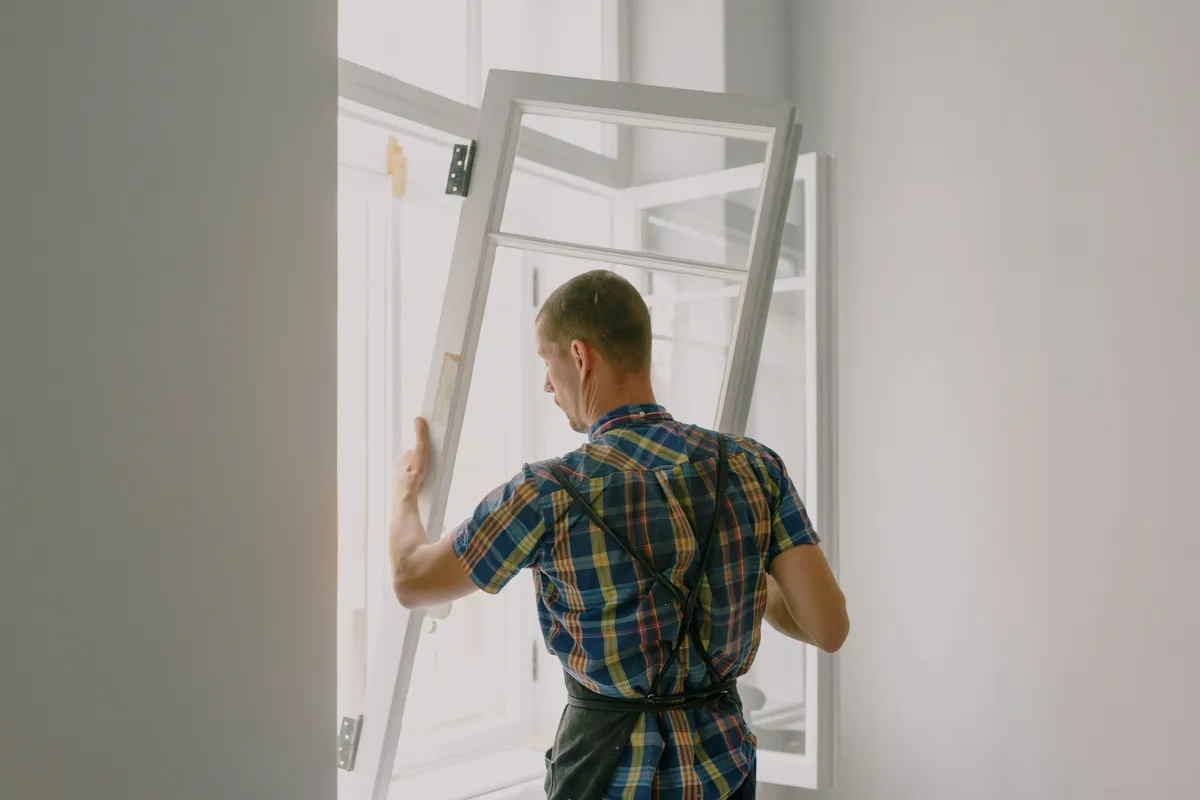 A worker fitting a new window unit during a renovation — whether the existing frame is sound enough for a pocket insert decides much of the installation labor.