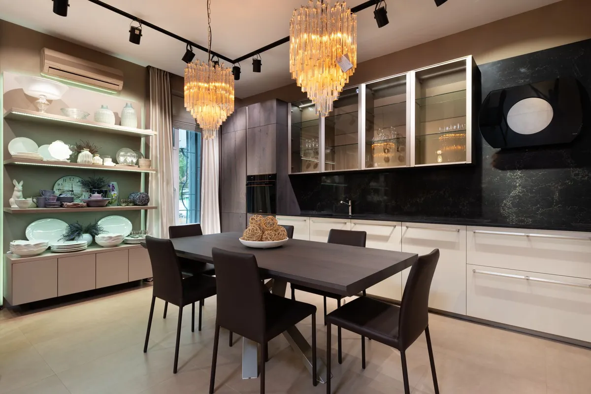 A showroom kitchen run with dark matte counters behind a dining area — decorative edges and integral sinks are fabricated into a zinc top at the quote stage, not added after, because the sheet is formed to one template. The pictured counters are not certified as zinc.